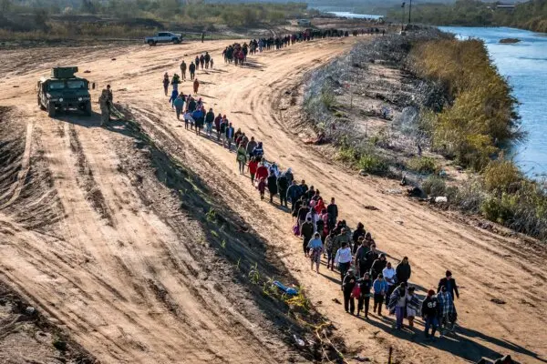 in this aerial view, A group of more than 1,000 illegal aliens walk towards a U.S. Border Patrol field processing center after they crossed the Rio Grande from Mexico in Eagle Pass, Texas, on Dec. 18, 2023. (John Moore/Getty Images)
