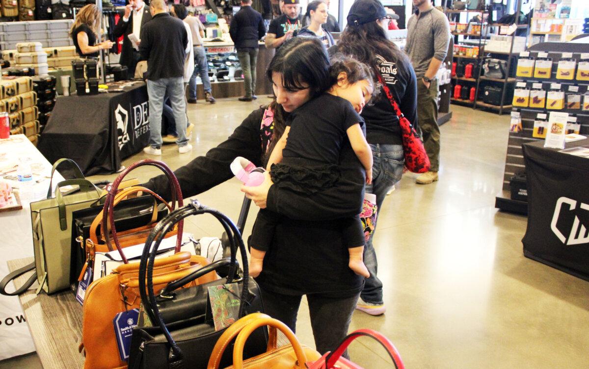 Rachel Sumler of Arlington, Texas, looks over concealed carry purses as her daughter naps during the National Women's Range Day event in Grapevine, Texas, on March 9, 2024. (Michael Clements/The Epoch Times)