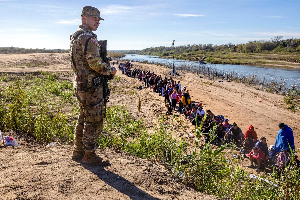 A Texas National Guard soldier watches over a group of more than 1,000 illegal immigrants who had crossed the Rio Grande from Mexico to Eagle Pass, Texas, on Dec. 18, 2023. (John Moore/Getty Images)