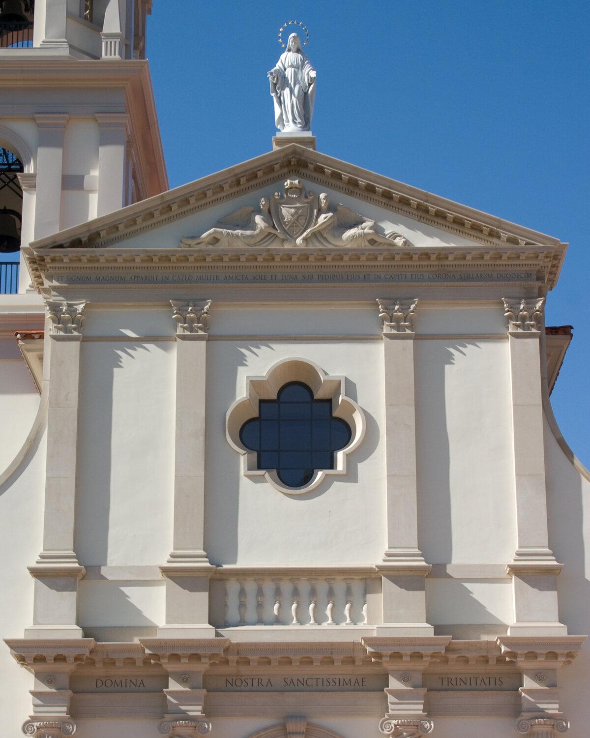 Above the main entrance, a classical temple face is adorned with four pilasters (engaged columns), a central quatrefoil (four-pointed) window, and a classical pediment topped by a sculpture of the Virgin Mary. Within the pediment is a bas-relief of the college's coat of arms flanked by two angels. (Courtesy of Thomas Aquinas College)