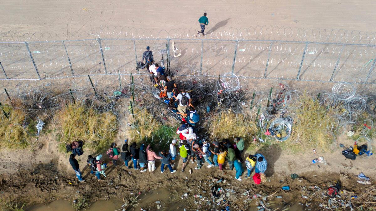 Illegal immigrants pass through coils of razor wire while crossing the U.S.–Mexico border in El Paso, Texas, on March 13, 2024. (John Moore/Getty Images)