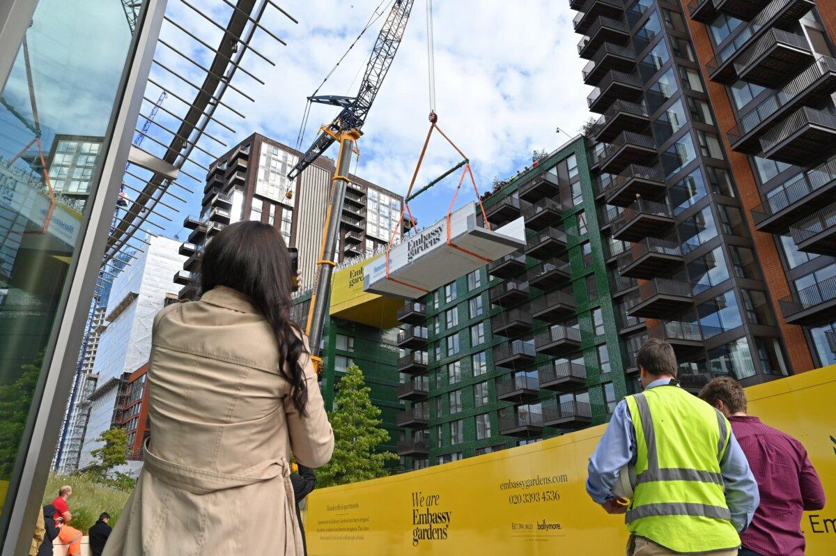 People gather to watch a crane lift a transparent acrylic swimming pool bridge that will be fixed between two apartment blocks at Embassy Gardens next to the new U.S. Embassy in southwest London on Sept. 28, 2020. (Justin Tallis/AFP via Getty Images)