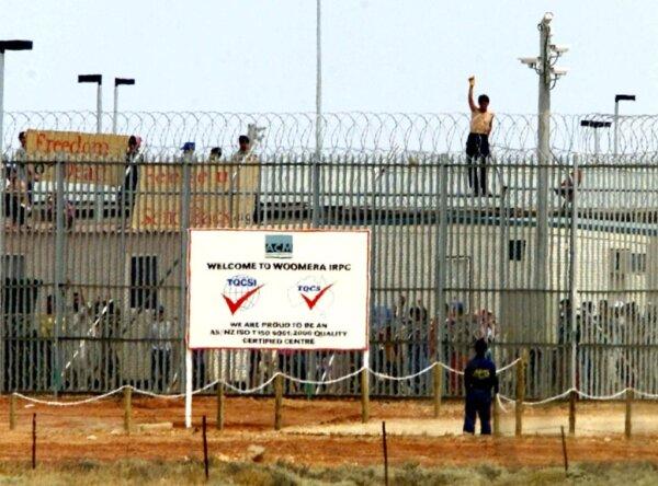 A detainee stands next to the razor wire fence (R) before he jumps and is seriously injured at the Woomera detention centre on 26 January 2000. The asylum seeker threw himself off the fence as others armed with metal bars attempted to break out. (Photo by AFP via Getty Images)