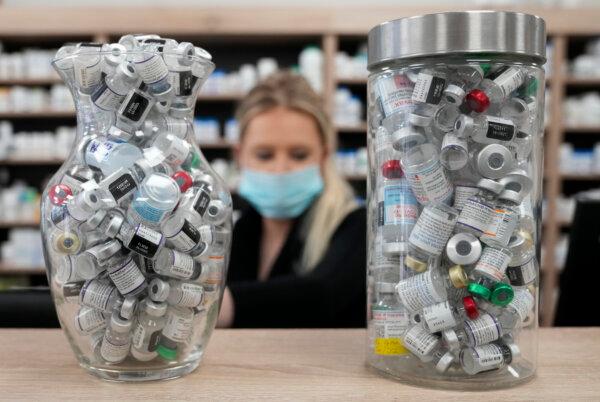 Jars containing empty COVID-19 vaccine vials are shown as a pharmacist works behind the counter at a pharmacy in Toronto on April 6, 2022. (The Canadian Press/Nathan Denette)