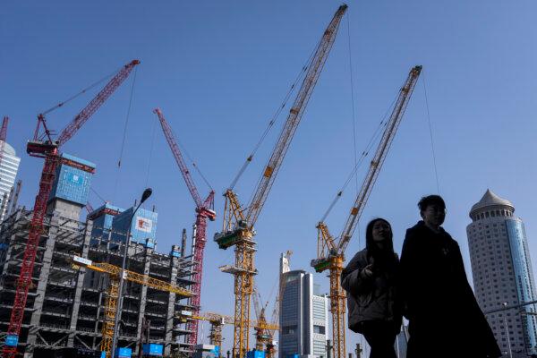 Un jeune couple marche devant un chantier de construction à proximité d’immeubles de bureaux dans le quartier central des affaires de Pékin, le 2 mars 2024. (AP Photo/Andy Wong)