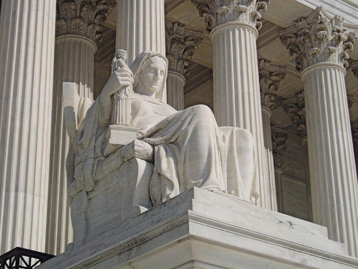 “Contemplation of Justice,” 1935, by James Earl Fraser, greets visitors beside the steps, at the entrance of the U.S. Supreme Court. The female figure rests one hand on a law book, and in the other she holds a statue of Justice blindfolded. (<a href="https://en.wikipedia.org/wiki/United_States_Supreme_Court_Building#/media/File:ContemplationOfJustice.JPG">Matt H. Wade/CC BY-SA 3.0 DEED</a>)
