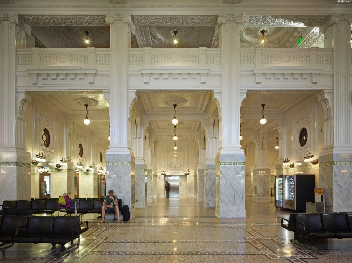 This view of King Street Station’s waiting area is a Gilded Age-era feast for the eyes, with its intricately molded coffered ceilings, second-floor gallery and balcony, and elaborate white marble and fluted Corinthian columns. Brass and globe lighting fixtures hang from ornately molded ceiling medallions. The simpler geometric design of the inlaid floor balances the overall lavish setting. (Courtesy Photographer Benjamin Benschneider)