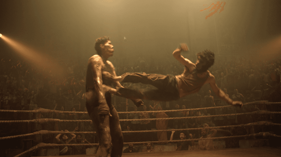 Kid (Dev Patel, right, wearing monkey mask) applies a flying kick in an underground MMA fight, in "Monkey Man." (Universal Pictures)
