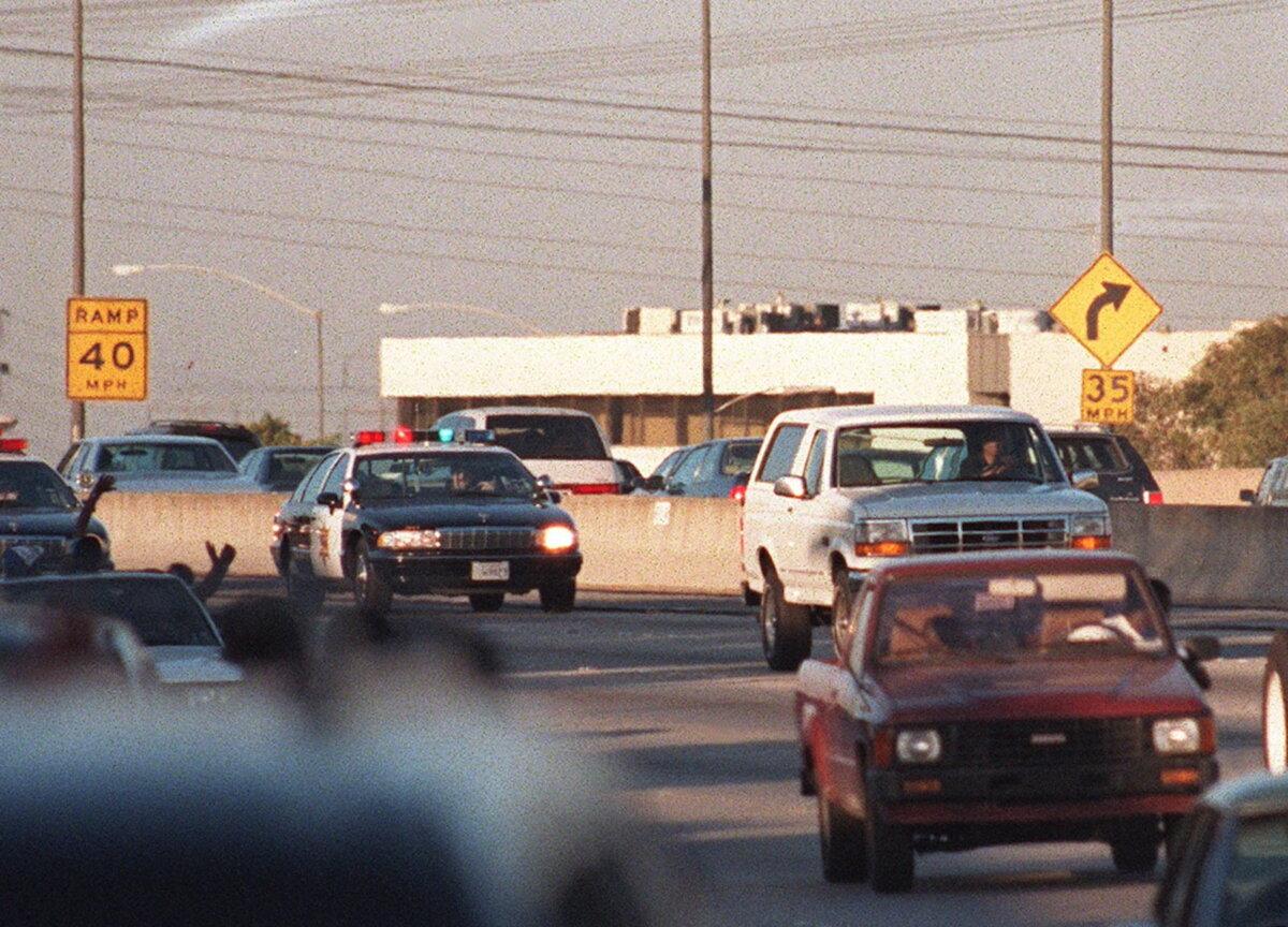 Motorists wave as police cars pursue the Ford Bronco (white, R) carrying fugitive and murder suspect O.J Simpson on a 90-minute chase on Los Angeles freeway 17 June 1994. The car driven by Mr. Simpson's friend Al Cowling eventually drove to Mr. Simpson’s home in Brentwood where he surrendered after a stand-off with police. (Mike Nelson/AFP via Getty Images)