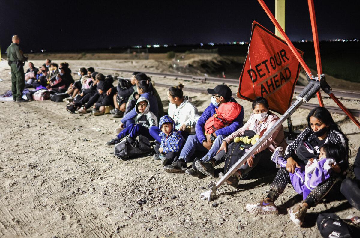 Illegal immigrants wait to be processed by Border Patrol agents after crossing from Mexico, with the U.S.–Mexico border barrier in the background, in Yuma, Ariz., on May 23, 2022. (Mario Tama/Getty Images)