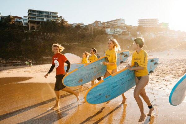 Adults enjoying a learn to surf experience with Manly Surf School at Freshwater Beach. (Courtesy of Destination NSW)
