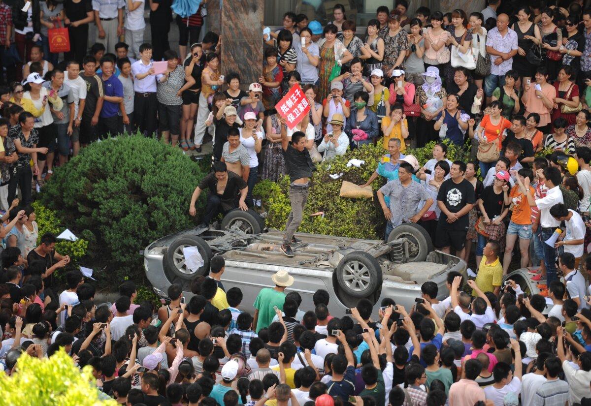 A man holds a placard as he stands on a car overturned by a group of protesters near the local government office compound in the coastal city of Qidong, near Shanghai, in eastern China's Jiangsu Province, on July 28, 2012. Thousands of demonstrators protesting against alleged pollution from a paper factory in east China clashed with police, an AFP photographer said. (Peter Parks/AFP/GettyImages)