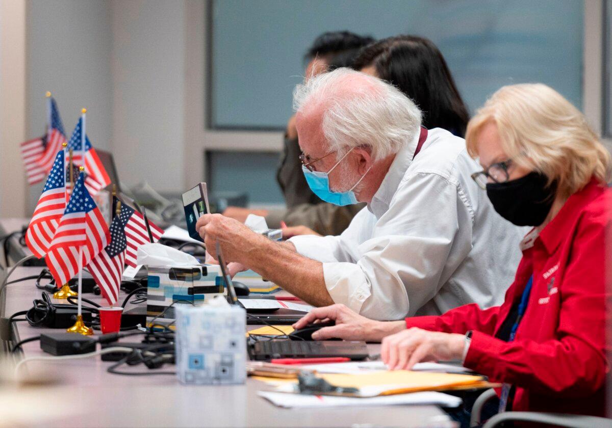 A man checks the ID of a voter before giving them a ballot at an early voting location in Fairfax, Va., on Sept. 18, 2020. (ANDREW CABALLERO-REYNOLDS/AFP via Getty Images)