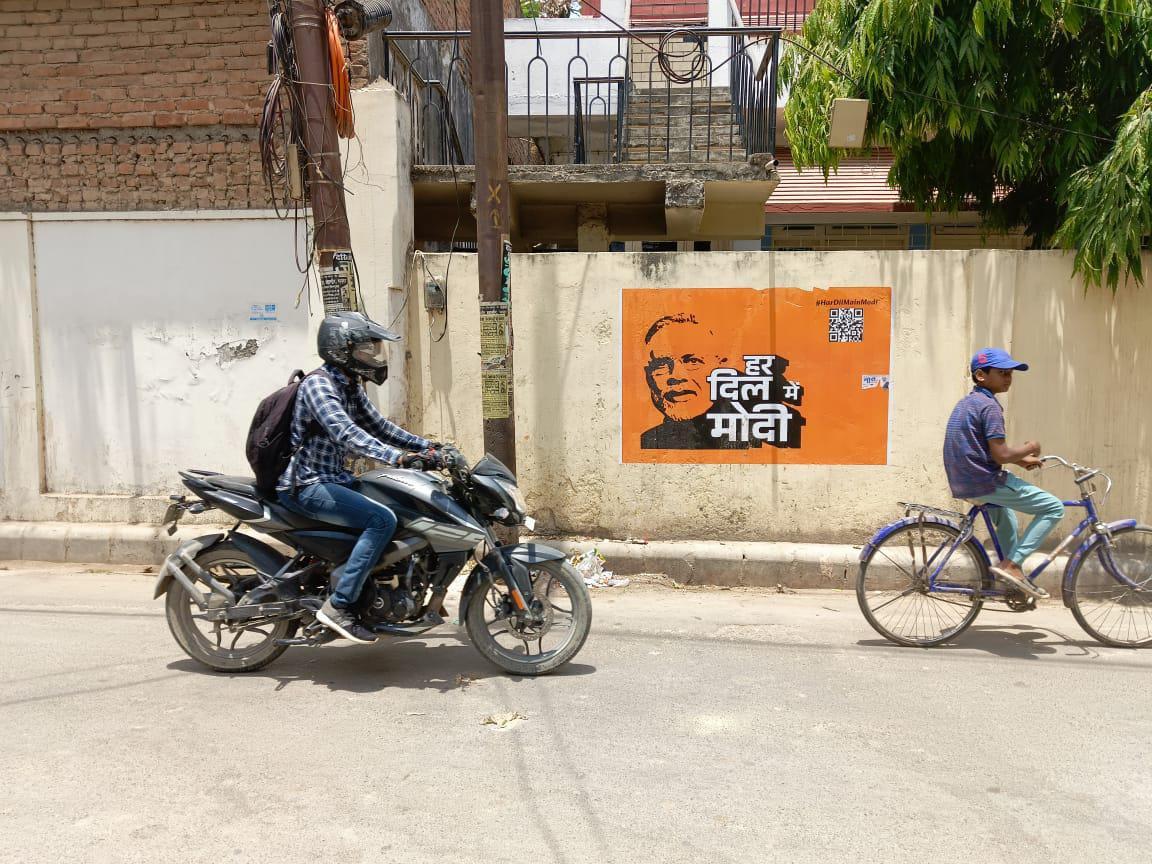 Riders pass an election poster of Indian Prime Minister Modi in the Navodit Nagar neighborhood of Varanasi on May 30, 2024. The poster says "Haar Dil Main Modi," meaning "Modi is in every heart" and gives a QR code for more information. (Venus Upadhayaya/The Epoch Times)