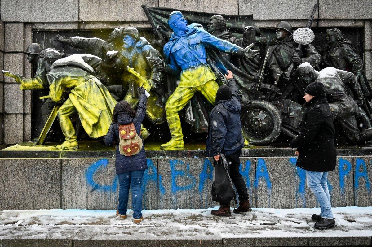 People paint the figures of Soviet soldiers using Ukranian flag colors at the base of the Soviet Army monument in Sofia, on Feb. 27, 2022. (Nikolay Doychinov/AFP via Getty Images)
