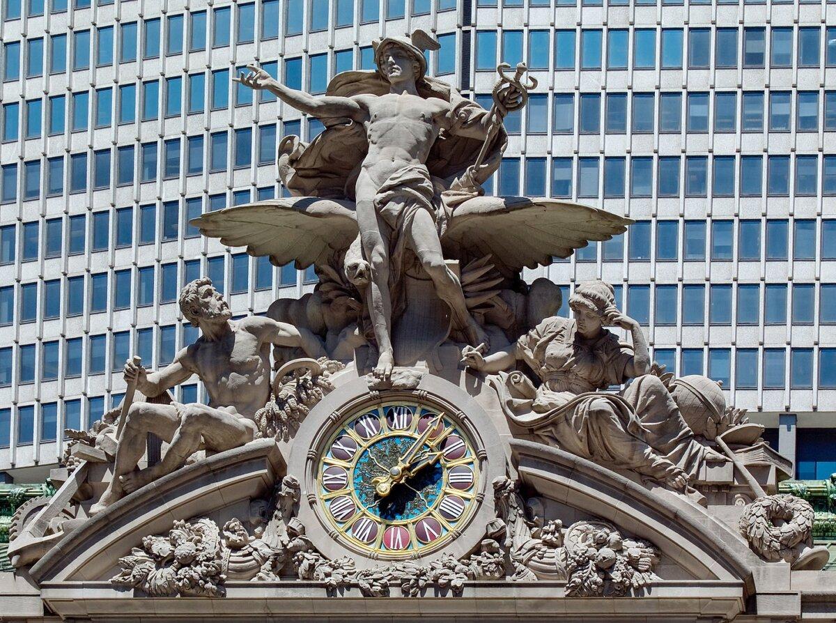 Glory of Commerce, a sculptural group by Jules-Félix Coutan, surrounds the sunburst-design clock. The god Mercury stands in the center above the world’s largest Tiffany-style stained-glass clock, at 13 feet in diameter. It is framed in bronze and has cast-iron clock hands. (Public Domain)
