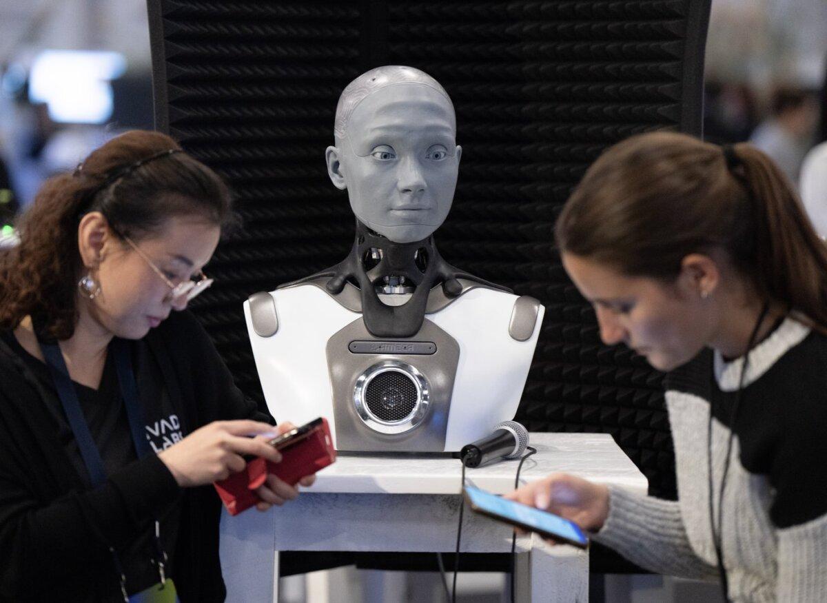 People check their phones as AMECA, an AI robot, looks on at the All In Artificial Intelligence conference in Montreal on Sept. 28, 2023. (Ryan Remiorz/The Canadian Press)
