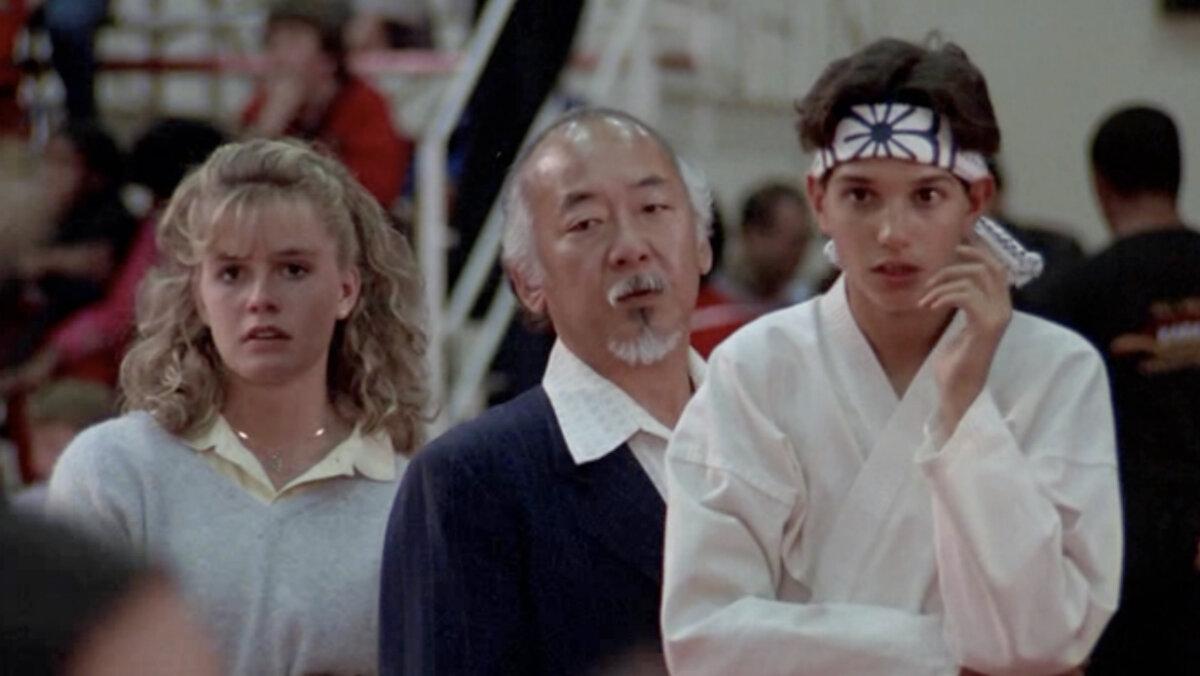 (L–R) Ali Mills (Elizabeth Shue), Miagi (Pat Morita), and Daniel LaRusso (Ralph Macchio) at the big tournament, in “The Karate Kid.” (Columbia Pictures)