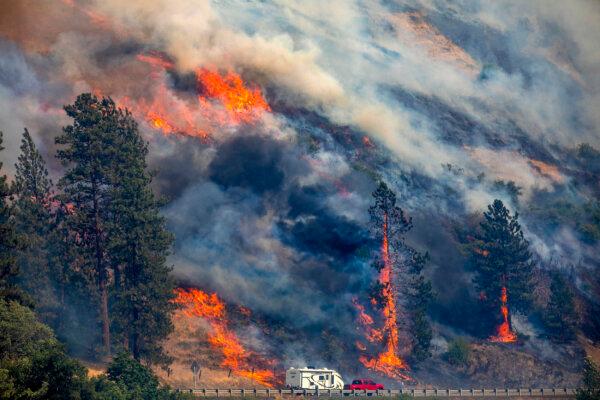 A vehicle drives past the spreading River Fire July 25, 2024, near Myrtle, Idaho, before U.S. Highway 12 was closed. Lightning strikes have sparked fast-moving wildfires in Idaho, prompting the evacuation of multiple communities. (August Frank/Lewiston Tribune via AP)