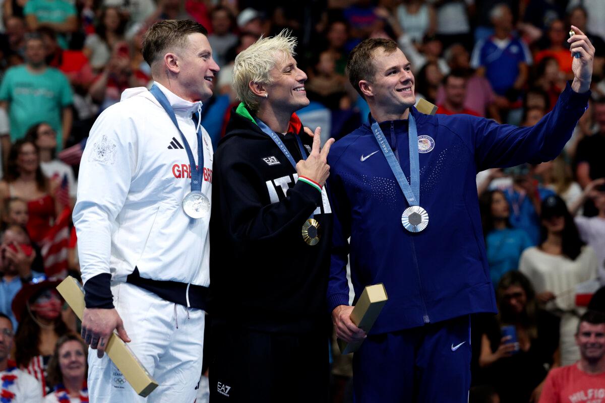 Gold Medalist Nicolo Martinenghi of Team Italy (C) and Silver Medalists Adam Peaty of Team Great Britain (L), and Nic Fink of Team United States (R) pose for a selfie on the podium during the Swimming medal ceremony after the Men’s 100m Breaststroke Final on day two of the Olympic Games Paris 2024 at Paris La Defense Arena Nanterre, France, on on July 28, 2024. (Quinn Rooney/Getty Images)