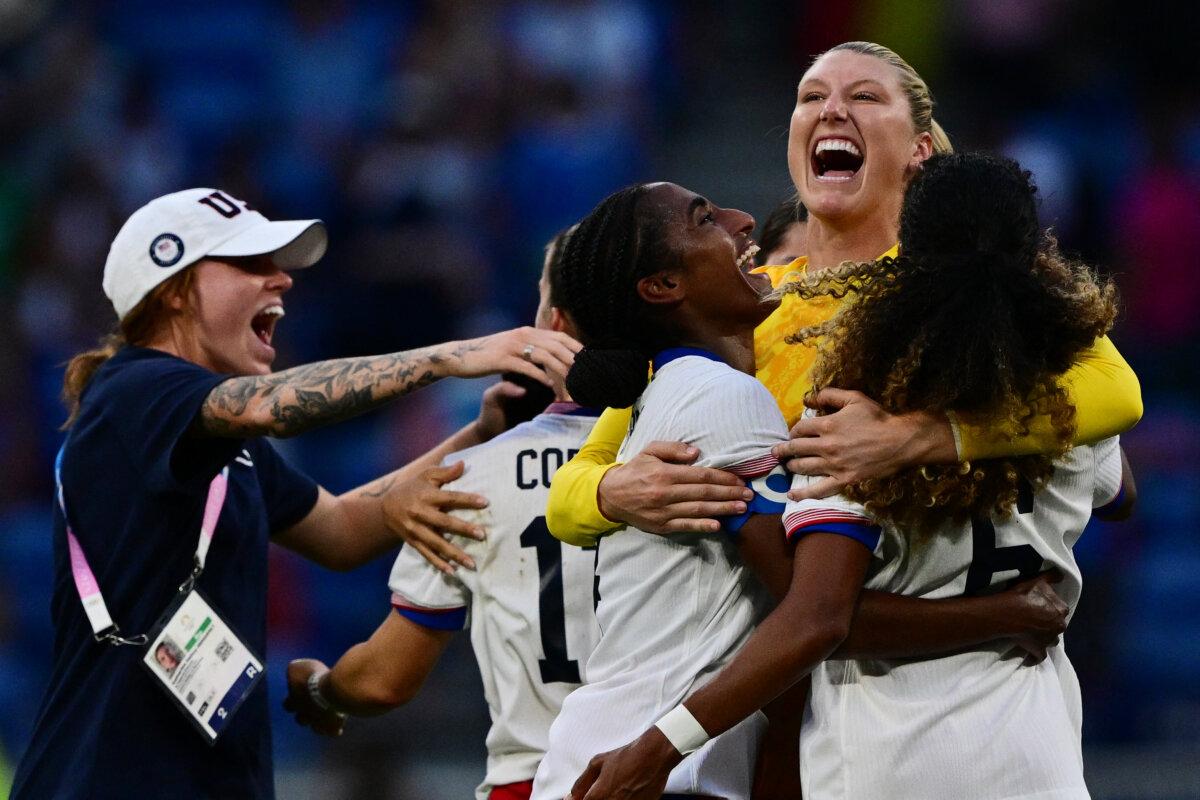 Team USA's goalkeeper Alyssa Naeher (2nd R) is embraced by defender Naomi Girma (3rd-R) and defender Casey Krueger (R) as they celebrate after the women's semifinal football match between the USA and Germany during the Olympic Games at the Lyon Stadium in Lyon, France, on Aug. 6, 2024. The USA won the game 1-0 after US forward Sophia Smith scored during extra time in the 95th minute. (Olivier Chassignole/AFP via Getty Images)