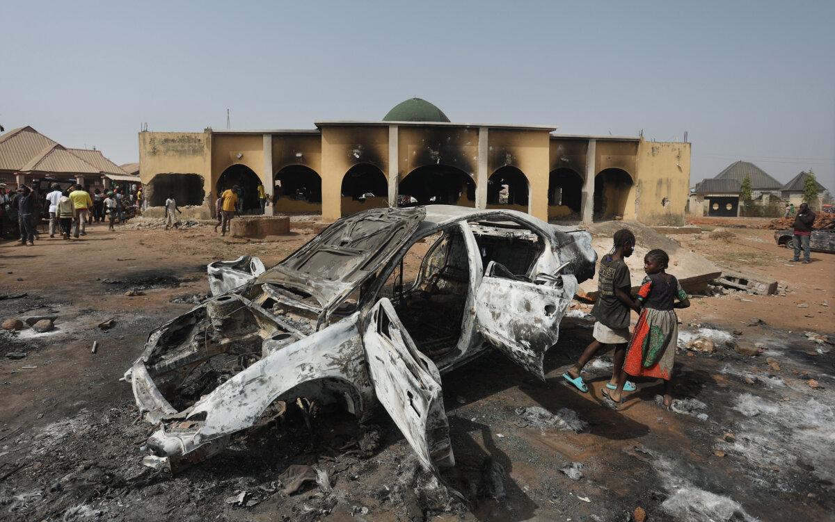 Two girls stand next to a burned car following weeks of violence and unrest in the Plateau State, at the Bungha Central Mosque in Mangu, Nigeria, on Feb. 2, 2024. (Kola Sulaimon/AFP via Getty Images)
