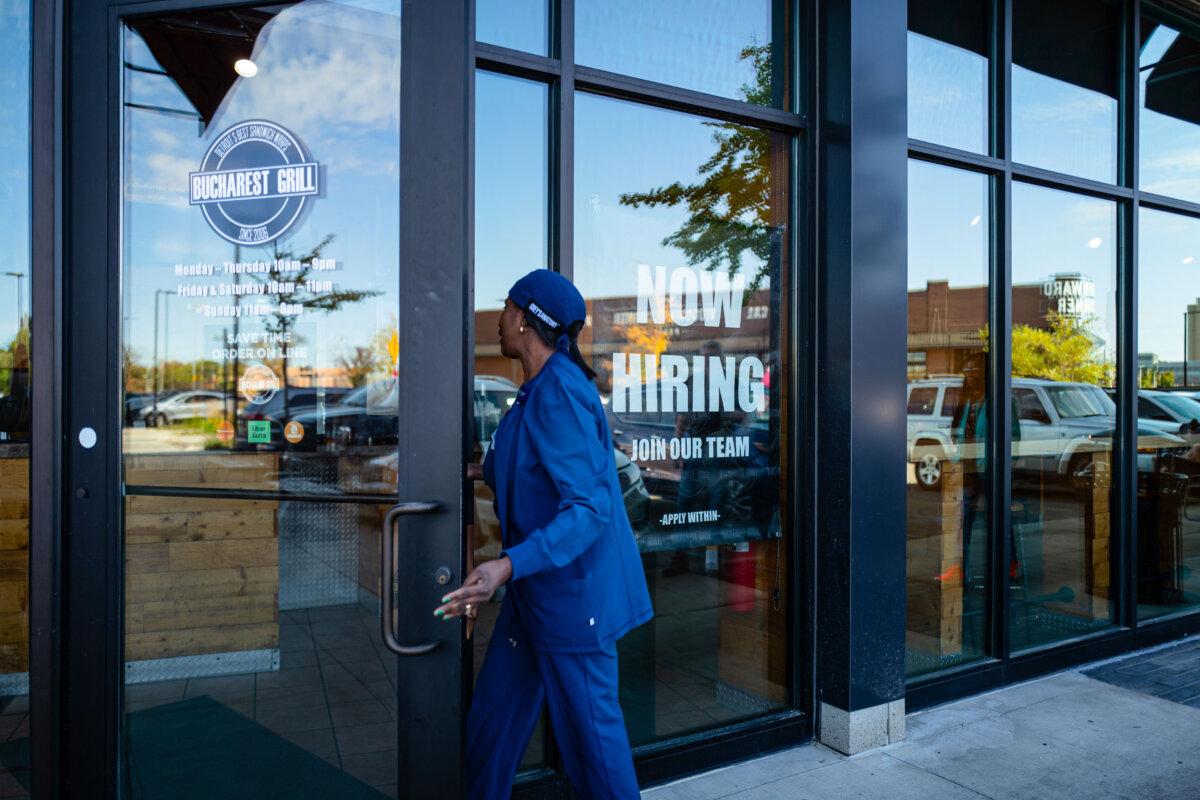A woman walks into a restaurant displaying a Now Hiring sign in Royal Oak, Mich., on Oct. 12, 2024. (Madalina Vasiliu/The Epoch Times)