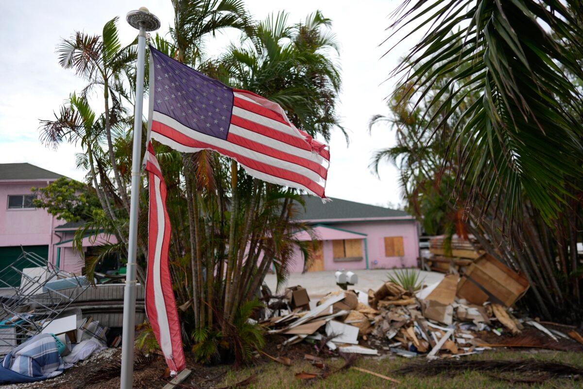 A tattered American flag flaps outside a home with furniture and household items damaged by Hurricane Helene piled outside along the street awaiting pickup ahead of the arrival of Hurricane Milton in Holmes Beach on Anna Maria Island, Fla., on Oct. 8, 2024. (Rebecca Blackwell/AP Photo)