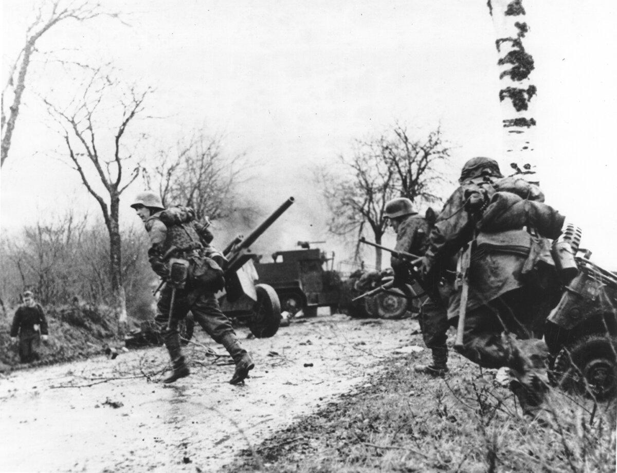 This photo from a captured Nazi shows German troops rushing across a Belgian road blocked with destroyed American jeeps and half-tracks from an enemy attack on Dec. 16th, 1944. National Archives at College Park. (Public Domain)
