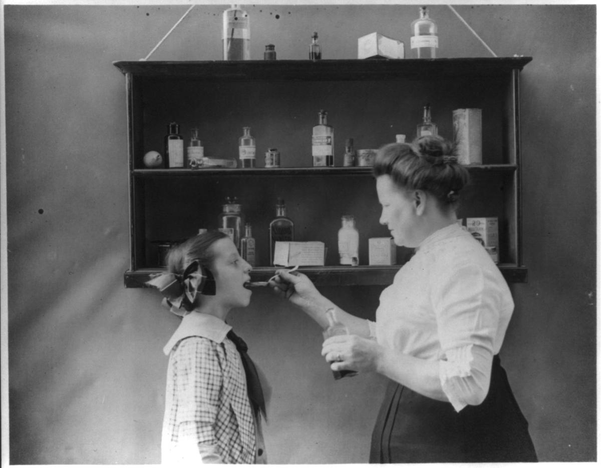 In this 1915 photograph, a mother gives medicine to her sick child. (Public Domain)