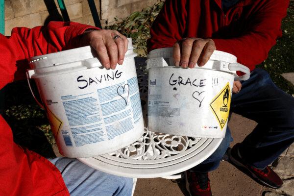 Neighbors Jason Salit and Billy Malone sit holding buckets that read "Saving" and "Grace", as the Eaton Fire continues, in Altadena, Calif., on Jan. 14, 2025. (Shannon Stapleton/Reuters)