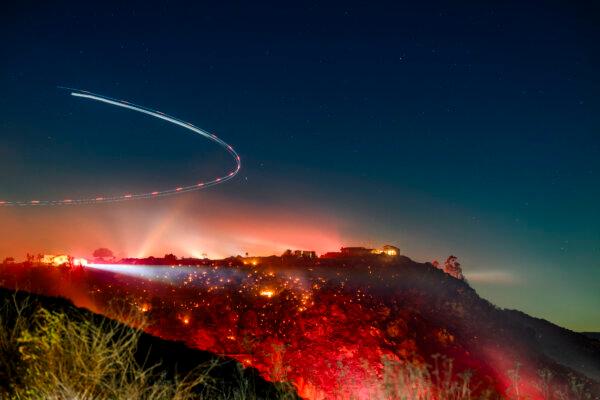 In this long exposure photo, a helicopter investigates a scene during an unedited lilac fire in San Diego County, California on January 21, 2025 (photo by Josh Edelson/AFP via Getty Images)