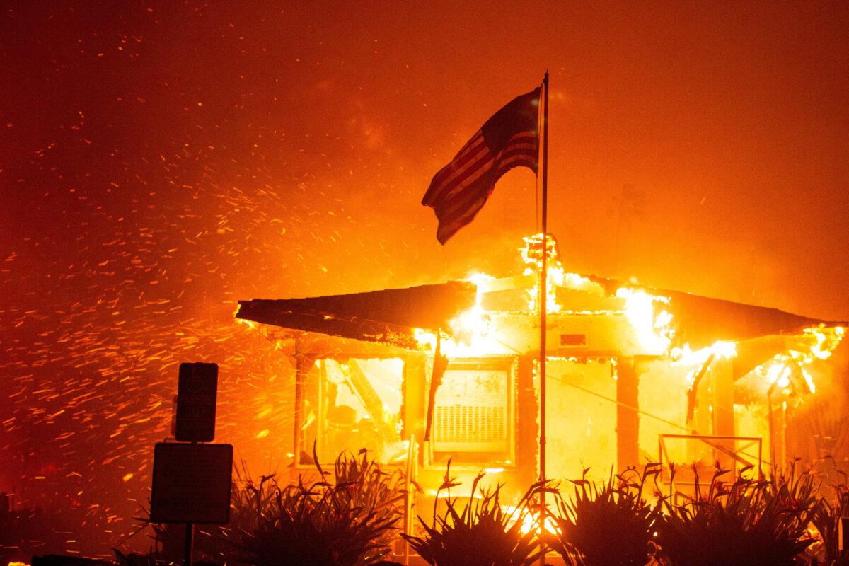 A U.S. flag flies as fire engulfs a structure while the Palisades fire burns during a windstorm on the west side of Los Angeles on Jan. 7, 2025. (Ringo Chiu/Reuters)