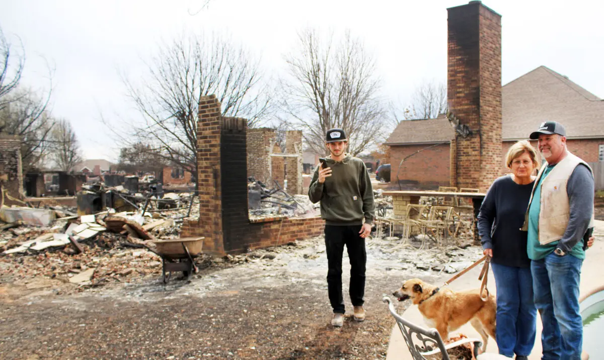 Jay Caffey (R), his mother-in-law Beth, his dog Charlotte, and his friend Max stand in front of his burned out house in Stillwater, Okla., on March 15, 2025. (Michael Clements/The Epoch Times)