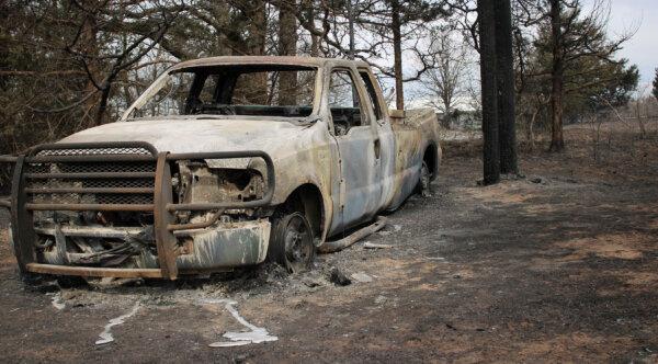 The charred remains of a pickup truck sit in the scorched woods off Douglas Road in Guthrie, Okla., on March 15, 2025. (Michael Clements/The Epoch Times)