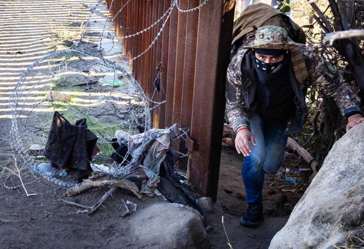 A masked migrant illegally crosses into the United States outside of San Diego on Dec. 5, 2023. (John Fredricks/The Epoch Times)
