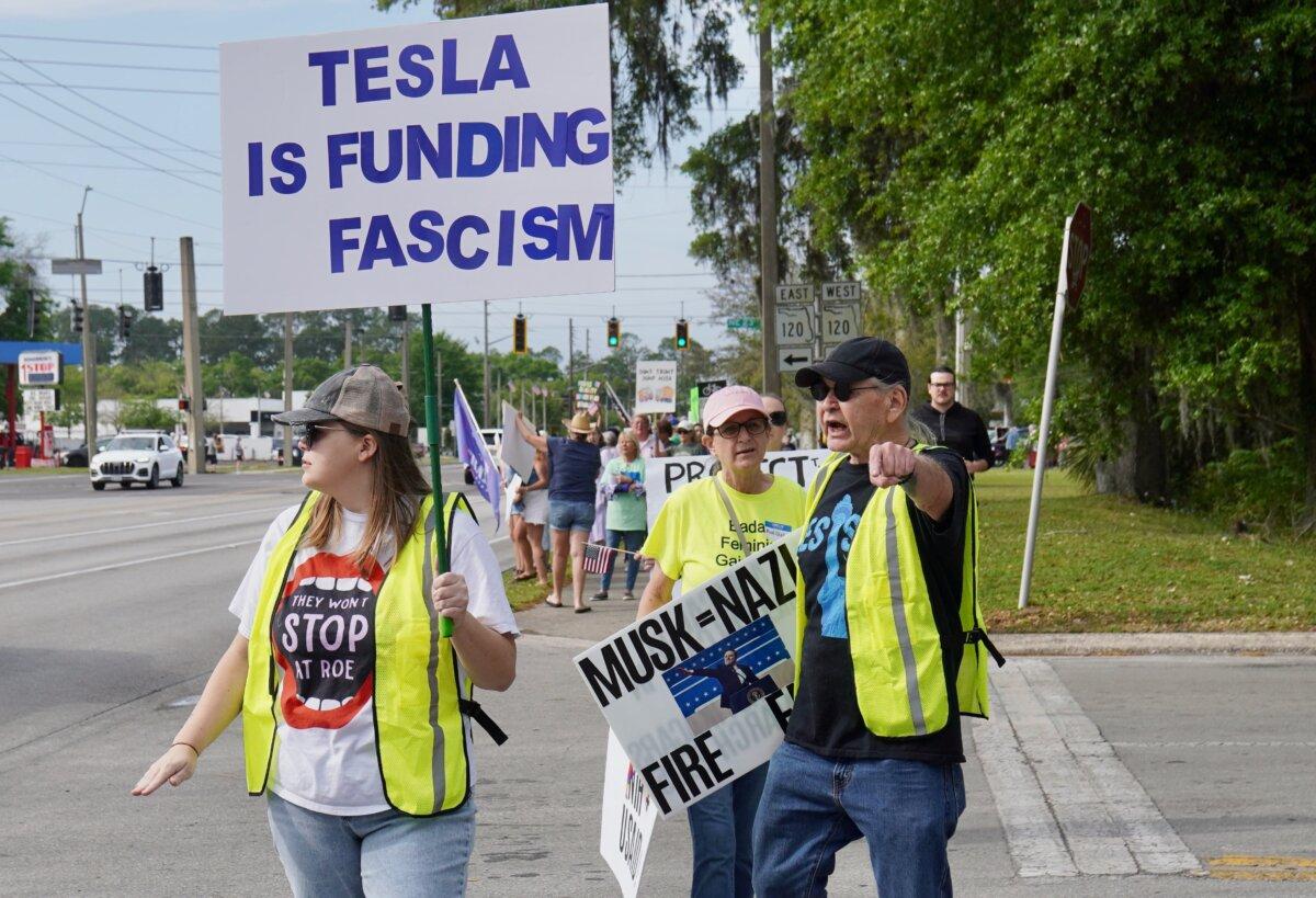 Jay Willard (right) participates in a protest with about 150 others across from a Tesla dealership in Gainesville, Fla., on March 29, 2025. (Nanette Holt/The Epoch Times)