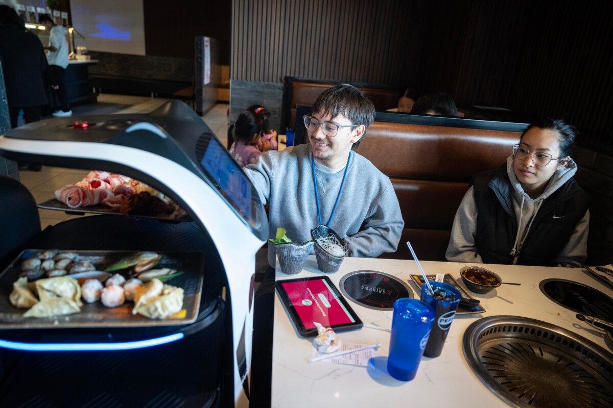 Webster Denison, left, and Jessica Yang, right, retrieve their food from a robot server at Shinhwa Korean Steakhouse in Roseville, Minnesota, on Tuesday, March 11, 2025. (Leila Navidi/The Minnesota Star Tribune/TNS)