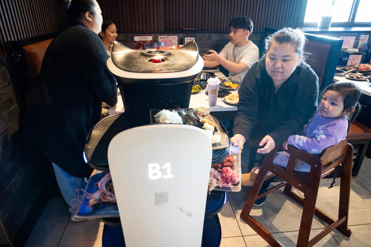 Mai Moua retrieves food from the robot server as her daughter Celine Yang, 2, looks on at Shinhwa Korean Steakhouse in Roseville, Minnesota, on Tuesday, March 11, 2025. (Leila Navidi/The Minnesota Star Tribune/TNS)