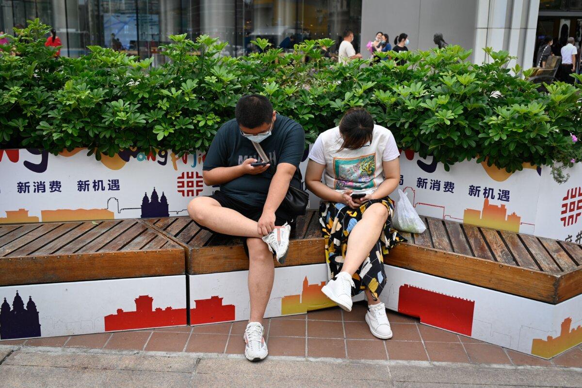 A couple use their mobile phones as they rest on a bench along a business street in Beijing on Sept. 15, 2021. (Wang Zhao/AFP via Getty Images)