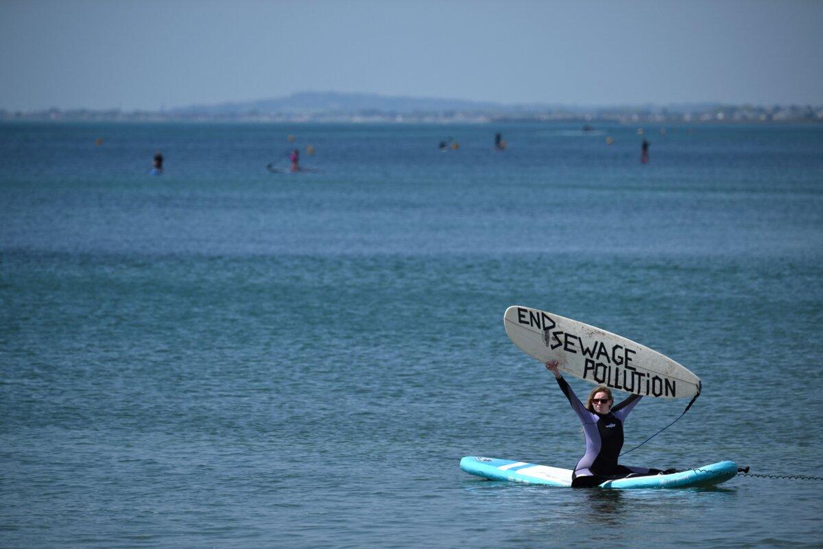 A Surfers Against Sewage activist holds a board reading "End sewage pollution" during a protest in Brighton, southern England, on May 20, 2023. (Ben Stansall/AFP via Getty Images)