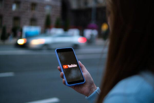 A woman holds a phone displaying the Youtube app, in this file photo, on Aug. 11, 2024. (Oleksii Pydsosonnii/The Epoch Times)