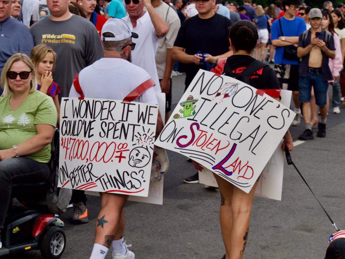 Dozens of protesters walk among thousands of spectators in line on Constitution Ave. for the Army's 250th anniversary parade in Washington, D.C., on June 14, 2025. (Travis Gillmore/The Epoch Times)