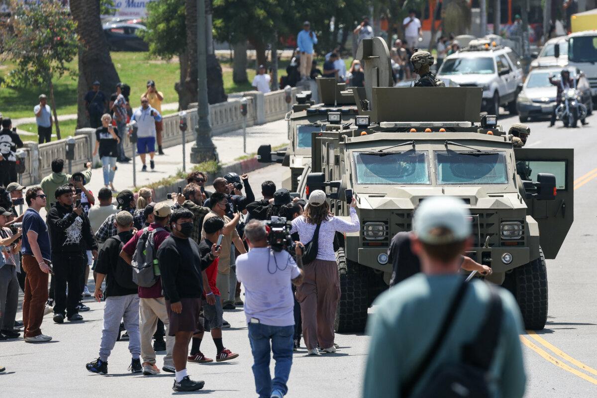 Crowds watch as federal agents with U.S. Customs and Border Patrol ride on an armored vehicle driving slowly down Wilshire Boulevard near MacArthur Park in Los Angeles, on July 7, 2025. (Patrick T. Fallon/AFP via Getty Images)