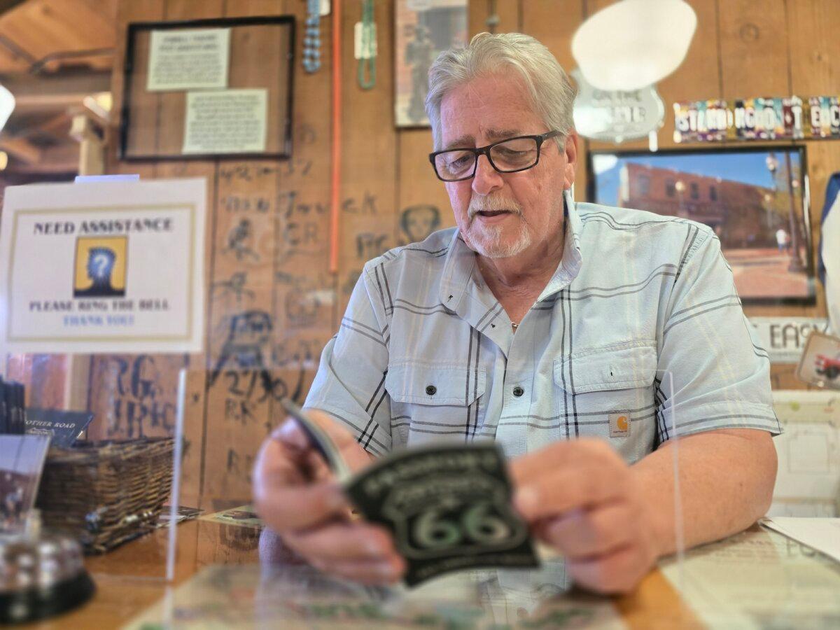 Rob Hall, CEO of the Winslow Chamber of Commerce and Visitor Center in Winslow, Ariz., thumbs through an Arizona 66 commemorative passport on July 16, 2025. (Allan Stein/The Epoch Times)