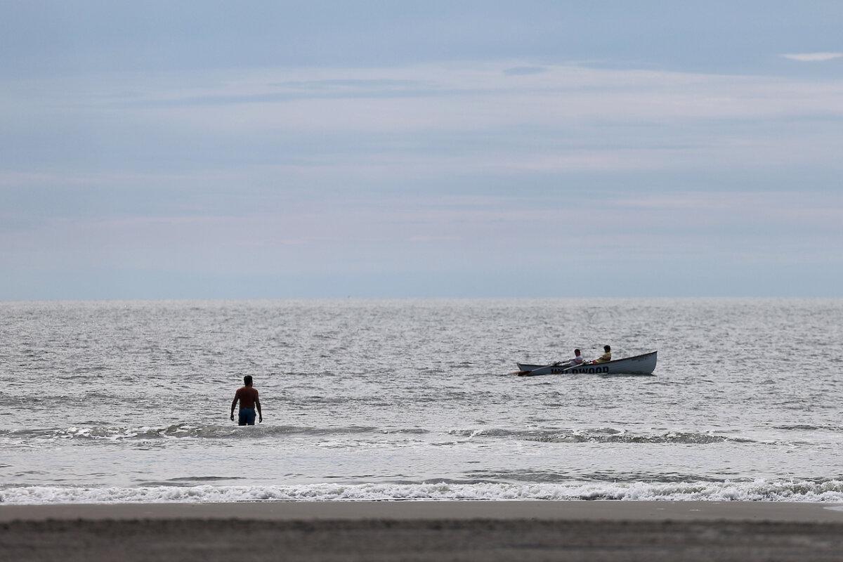 Dave Masi, of Wildwood Crest, takes a dip in the ocean as a lifeguard crew rows past in Wildwood May 26. (David Maialetti/The Philadelphia Inquirer/TNS)