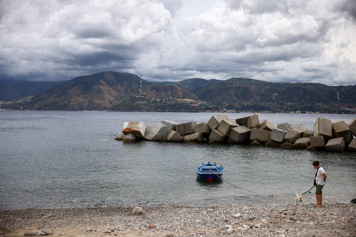 A woman walks with her dog along the Sicilian coast with the Italian mainland visible across the Strait of Messina, Italy, on Aug. 5, 2025. (Yara Nardi/Reuters)