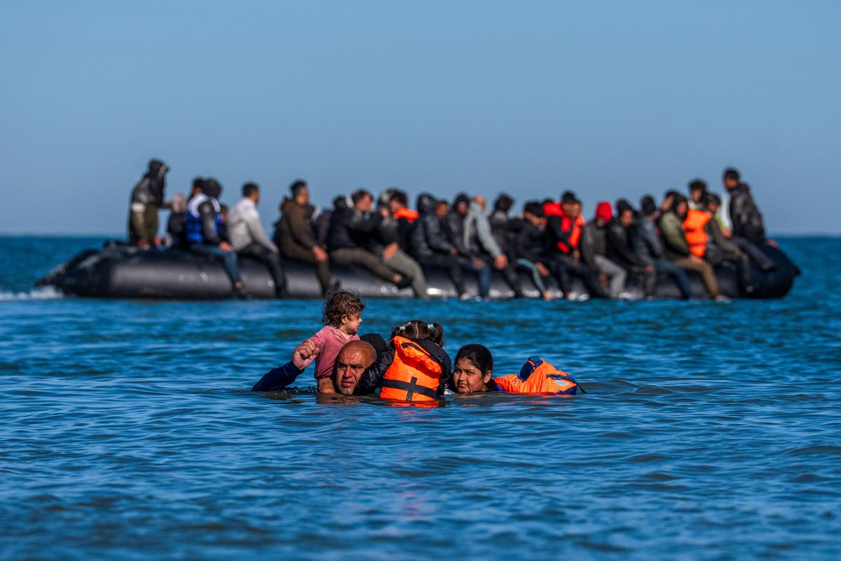 A girl is carried on a man's shoulders as migrants wade into the sea to try and board a dinghy to cross the English Channel in Gravelines, France, on Aug. 25, 2025. (Carl Court/Getty Images)