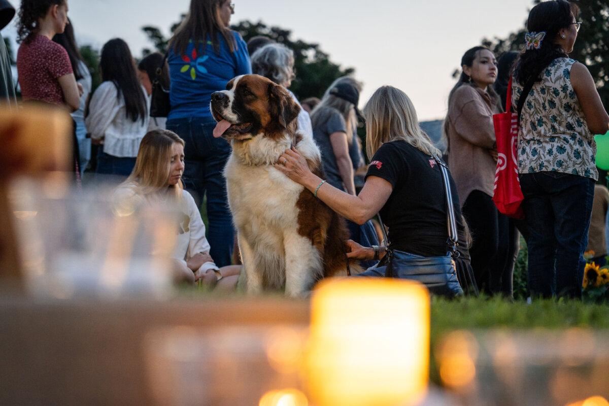 Kate Campo (R), a business owner in the neighborhood, sits with her dog, joining others in mourning the two schoolchildren who were killed a day before during the Annunciation Catholic School shooting in Minneapolis on Aug. 28, 2025. (Madalina Kilroy/The Epoch Times)