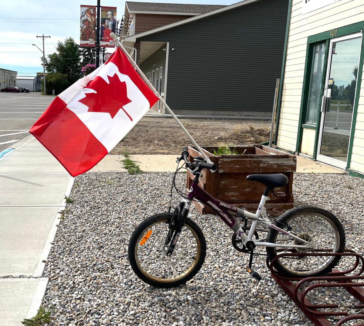 A bicycle with a Canadian flag sits outside a storefront in Didsbury, Alberta, on Aug. 21, 2025. (Allan Stein/The Epoch Times)